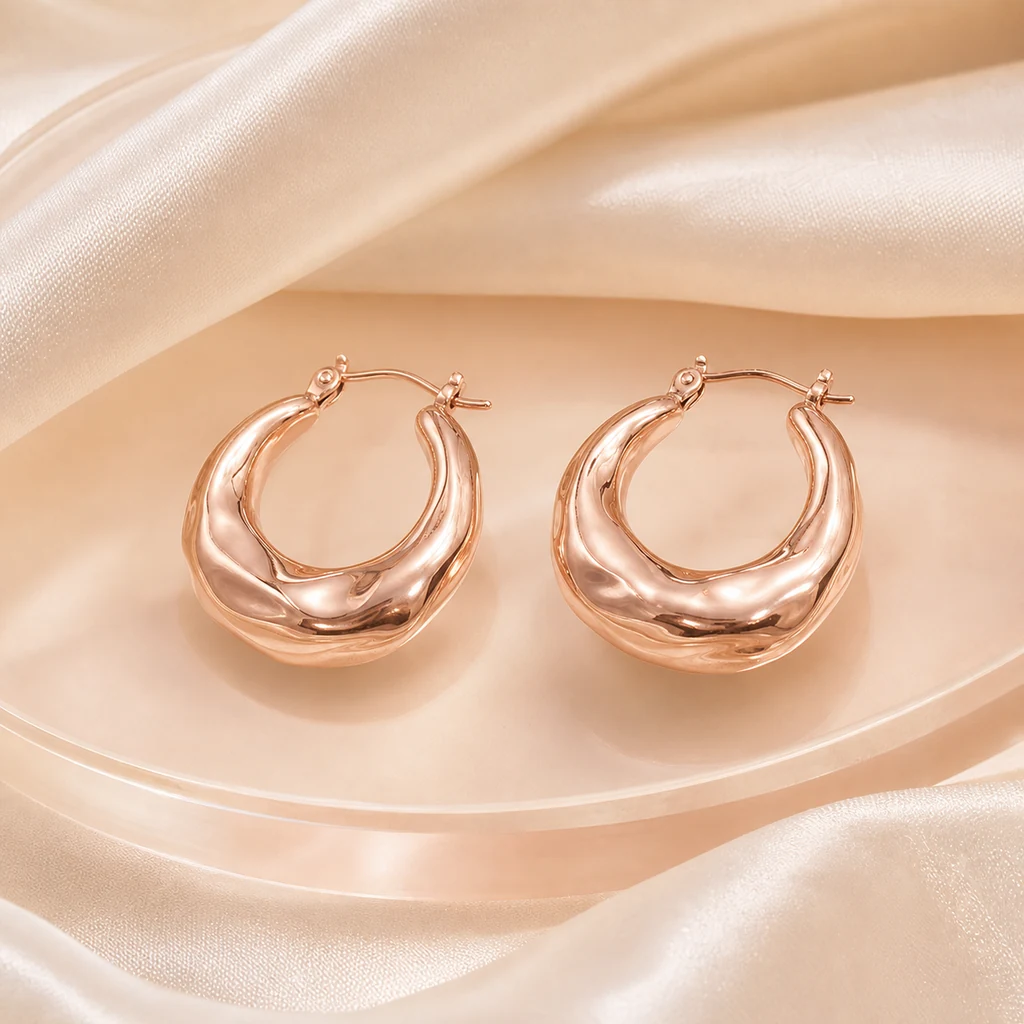 Rose-gold crescent hoop earrings on cream silk
